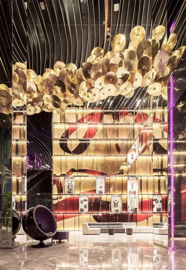 A modern hotel lobby adorned with metallic plates hanging from the ceiling and a curved glass wall.