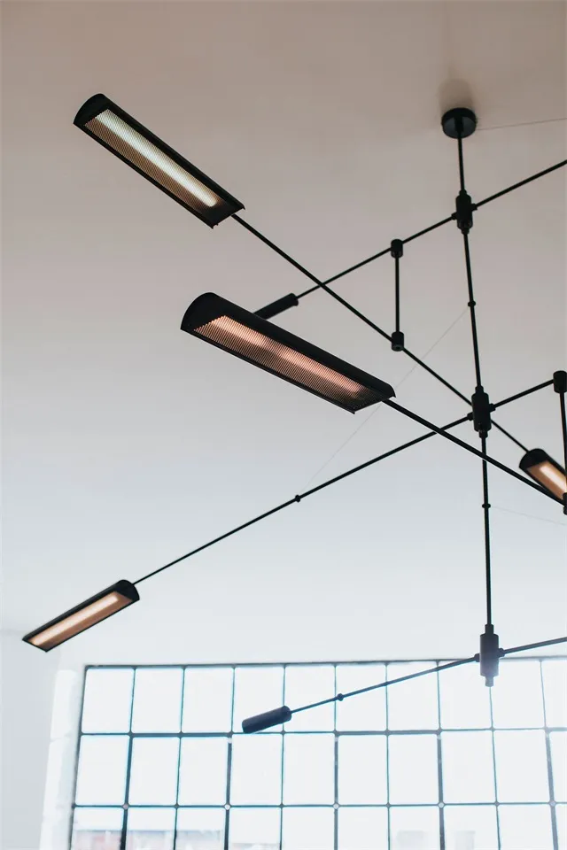 Modern industrial-style office ceiling lights hanging from metal wire framing system.