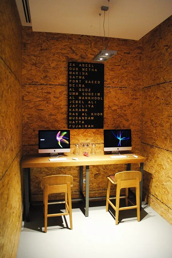 A modern, minimalist interior workspace featuring a wooden table with two computers and stools.