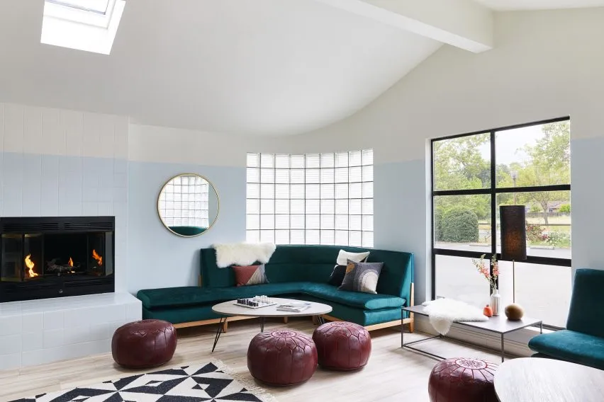A modern living room featuring a blue velvet couch, round coffee table, and concrete floor with geometric rug, illuminated by