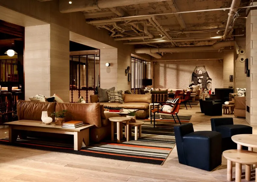 Modern lounge area with leather sofas, wooden tables, and concrete flooring in a hotel setting