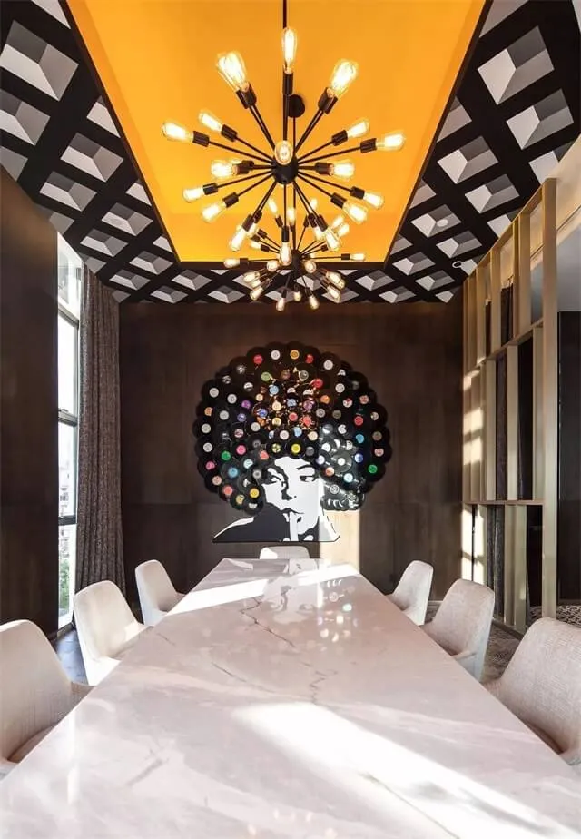 A modern dining room with a long marble table and chairs, industrial-style chandelier, and abstract wall art of a woman with