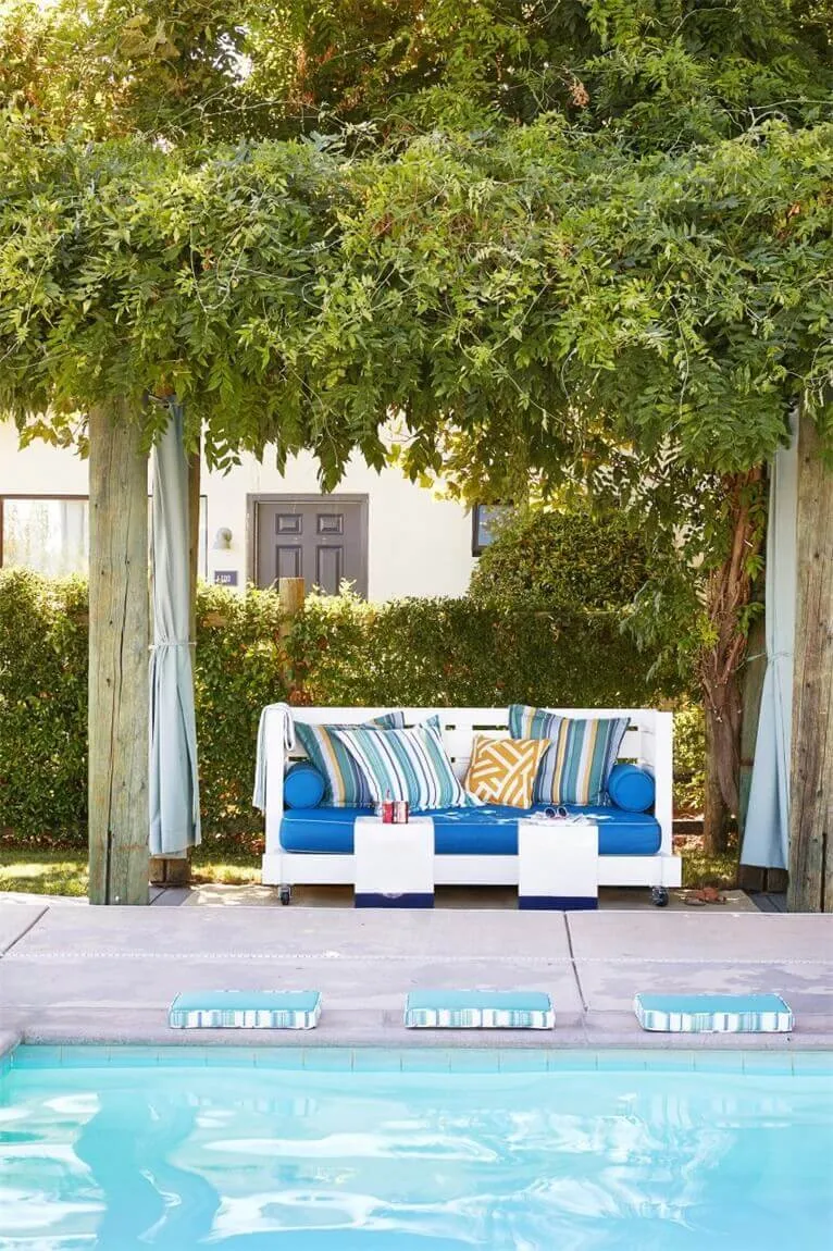 Modern outdoor furniture set near a poolside with blue cushions and striped pillows.