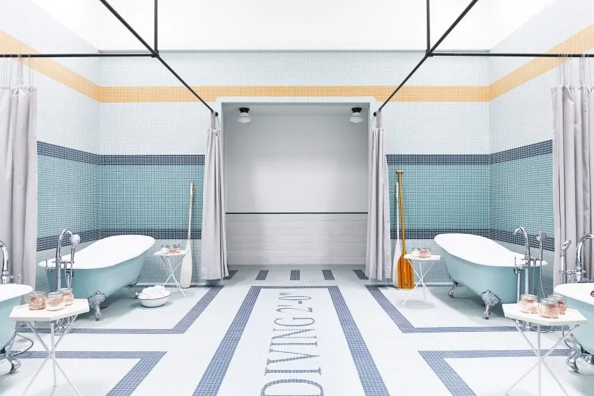 Modern public baths with blue clawfoot tubs, showers, and blue and white tiled floors.