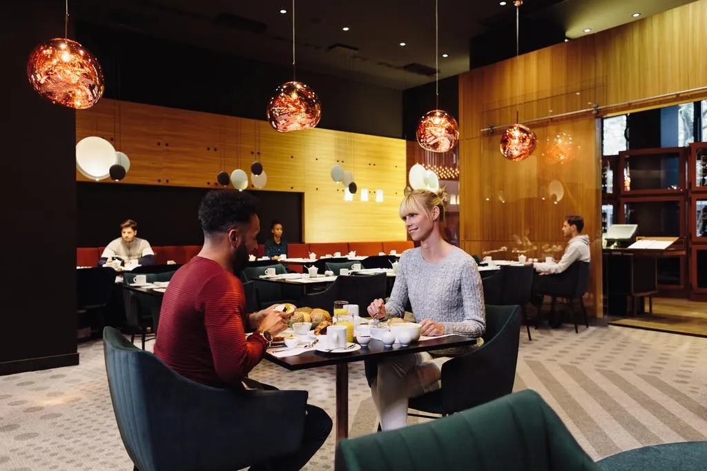 現代餐廳室內,客人坐在餐桌旁,搭配當代燈具與木質牆面。