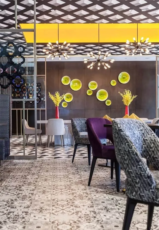Modern restaurant interior with checkered floor, geometric ceiling pattern, and yellow decorative elements.