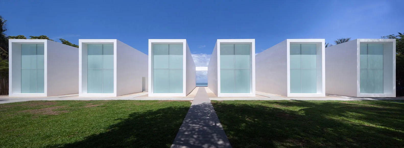 Minimalist architectural design featuring large white glass windows with a paved walkway and green lawn.