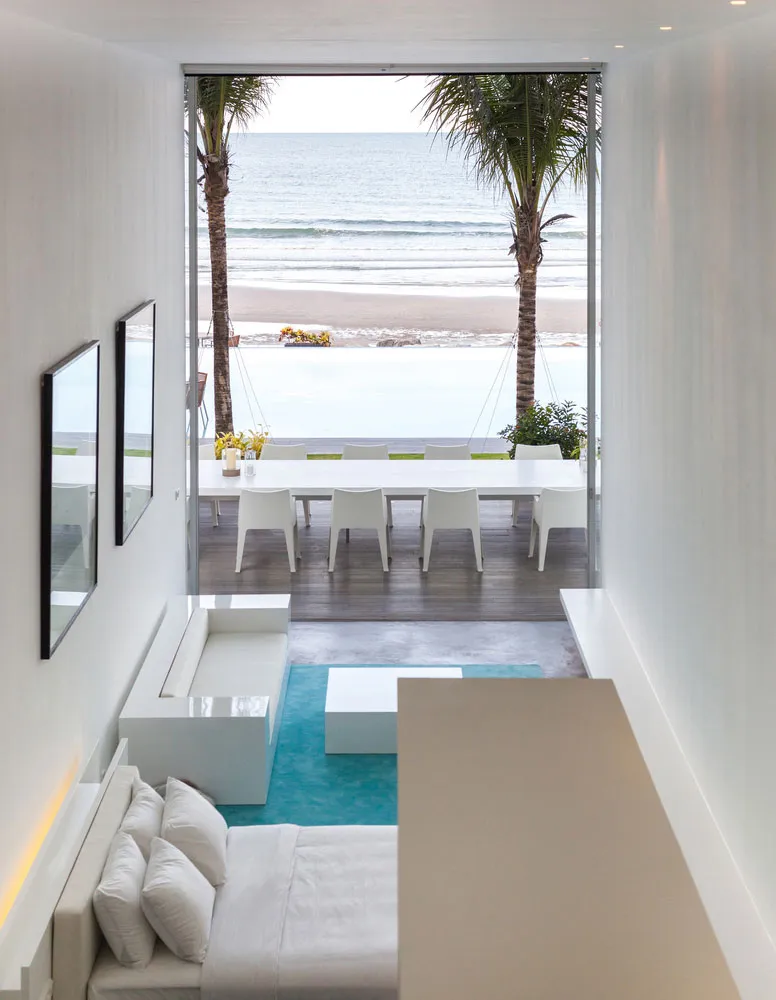 A minimalist white interior with a large glass window overlooking the sea.