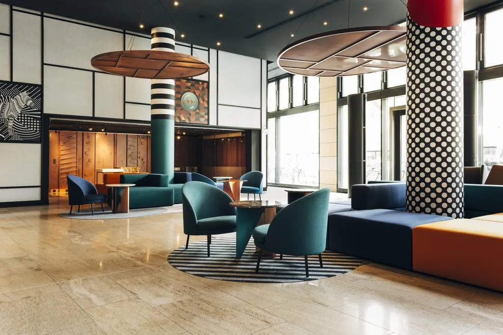 Modern office space featuring concrete columns, leather chairs, metal accents, and glass partitions.