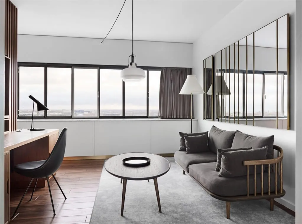 A minimalist living room with a grey sofa, wooden coffee table, and a large window.
