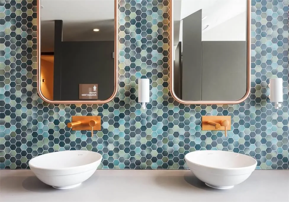 Modern bathroom with two white sinks, blue hexagonal tiles on the wall, and two rectangular mirrors.