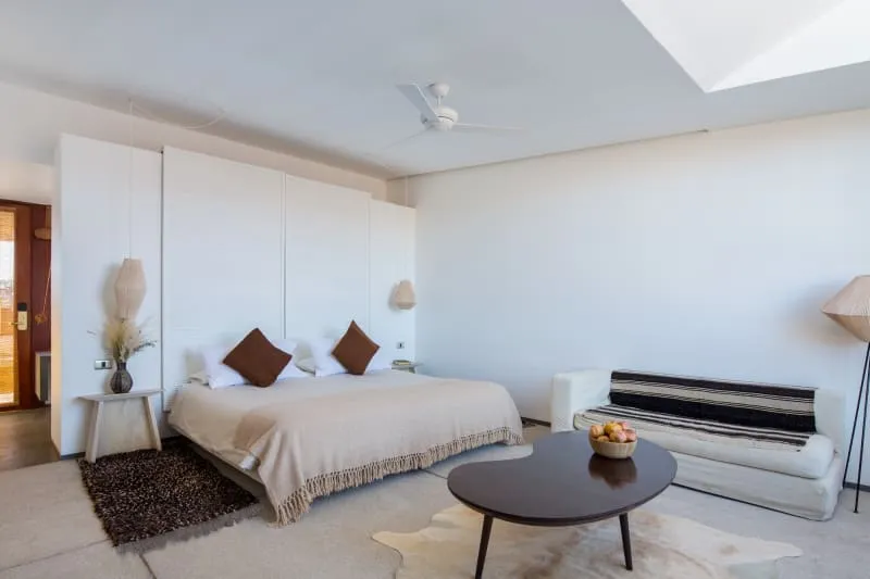 A modern bedroom with neutral-colored walls, a beige bedspread, and a white couch.