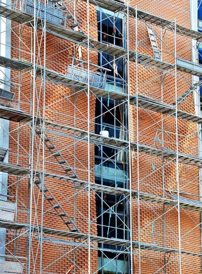 鋼製鷹架框架圍繞著一棟未完工的磚造建築物。