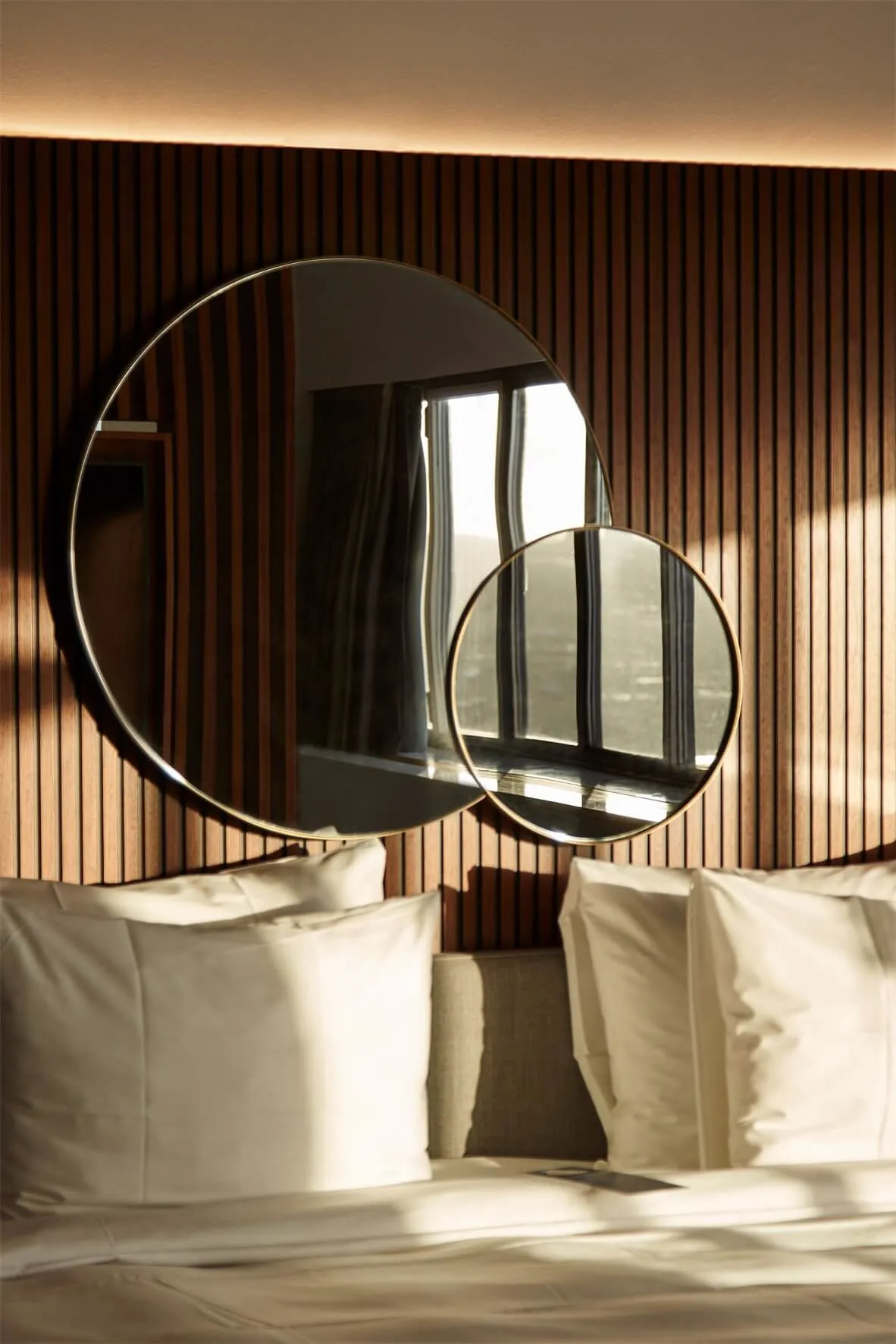 A minimalist bedroom with two circular mirrors mounted on a wooden wall, creating a modern and sleek atmosphere.
