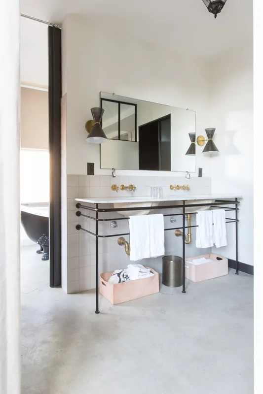 A modern bathroom with concrete flooring, white tiled walls, and a metal sink stand with a glass counter.