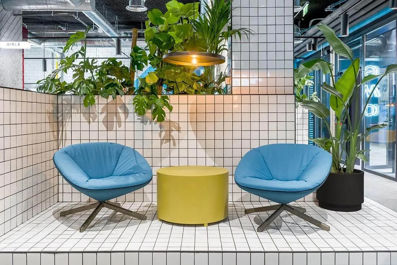 Modern coffee shop with blue fabric chairs on tiled floor, featuring a yellow central table and industrial-style light fixtur