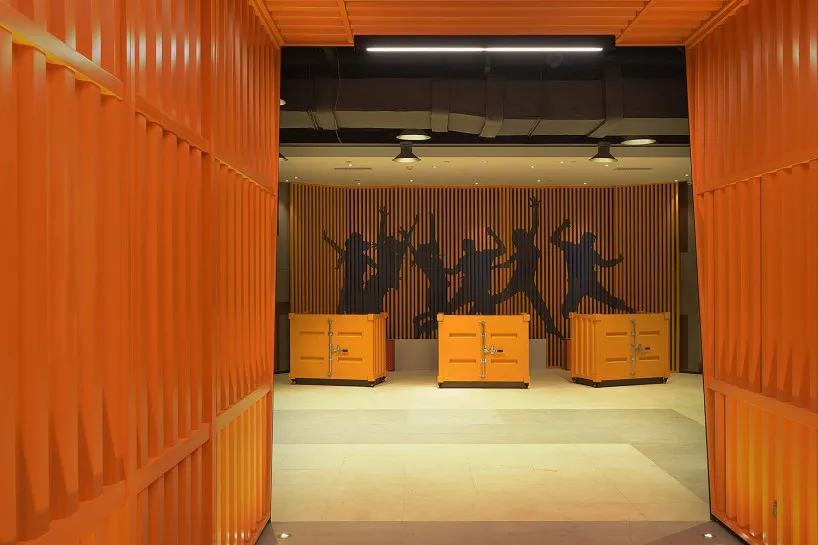 An indoor office corridor with modern industrial design featuring metal shipping container walls and orange accents.