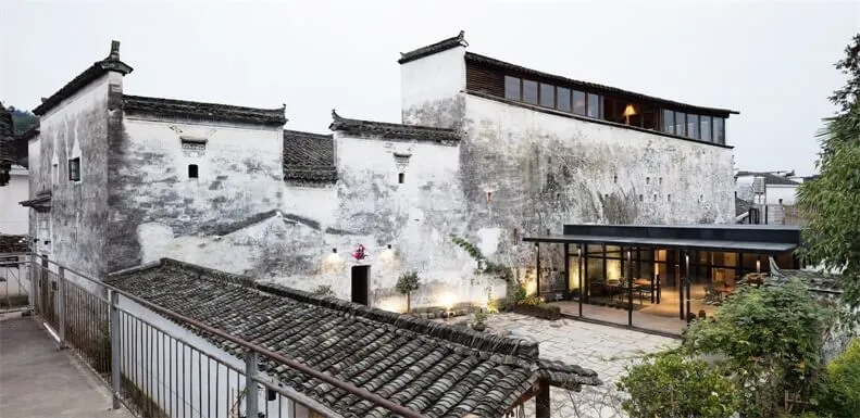 一棟白牆傳統中式民居,搭配現代混凝土與玻璃增建。