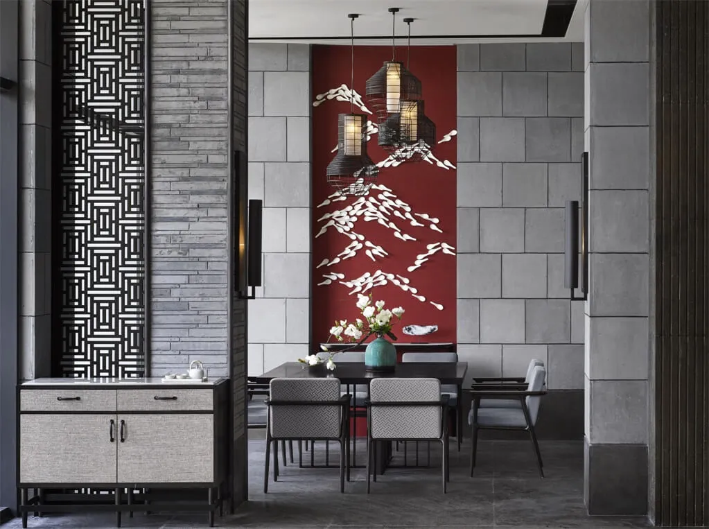 A modern dining room featuring a concrete wall, fabric upholstered chairs, and a large red artwork with white birds and lante