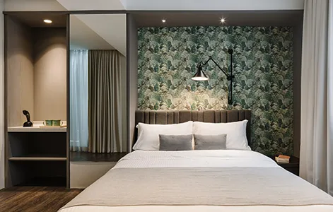 A modern minimalist bedroom featuring textured green and white geometric wallpaper, a white bed with white and grey pillows,