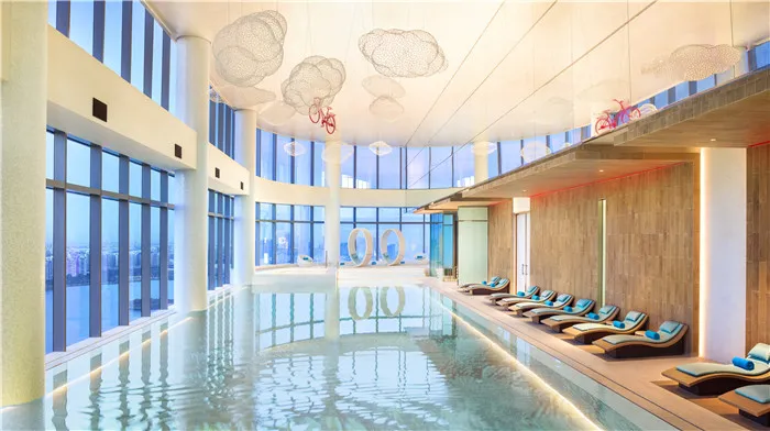 A minimalist indoor swimming pool with glass walls and a cloud-shaped light fixture.