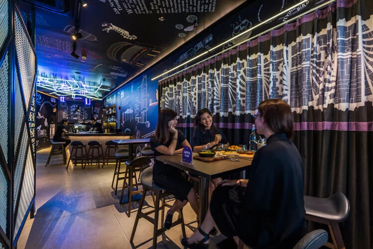 Three women sitting at a table in an industrial-style restaurant with metal, glass, and concrete elements.