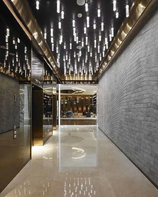 A modern corridor with concrete walls and floor, featuring cascading lights from the ceiling.