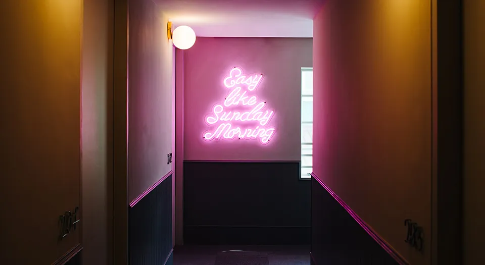 A pink neon sign with the phrase 'Easy like Sunday Morning' in a minimalist interior setting.
