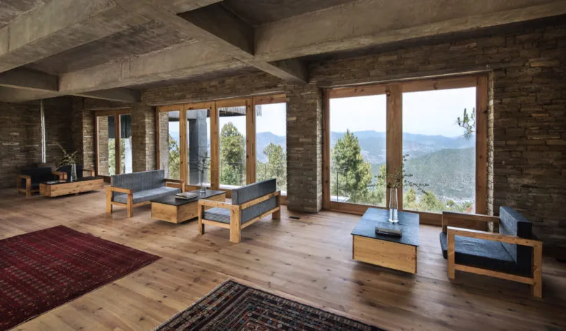 A modern living room with wooden floors, stone walls, and large windows overlooking mountains.