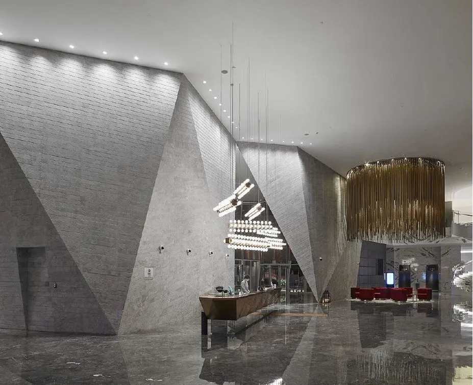 A modern lobby with concrete walls and ceiling, geometric lighting fixtures, and a reception desk.