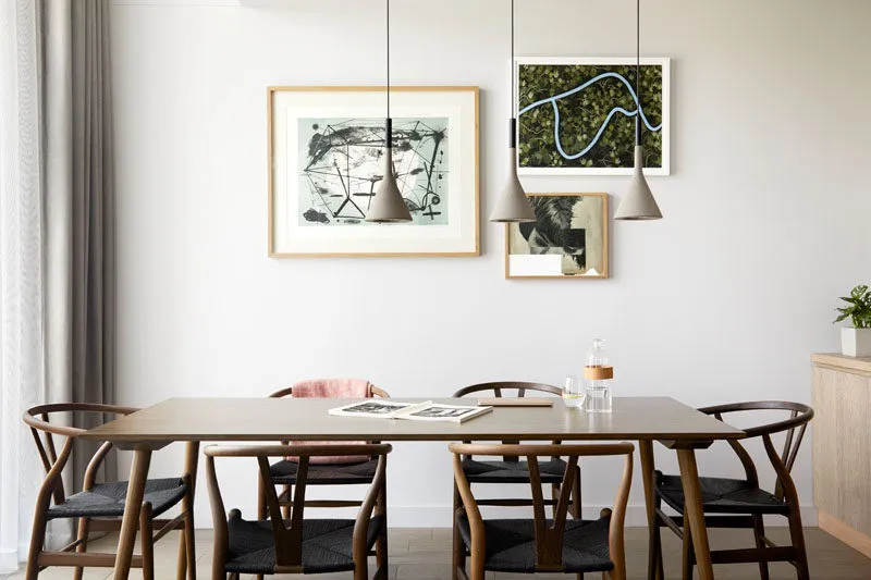 A modern minimalist dining room with a wooden table, black chairs, and concrete pendant lights.