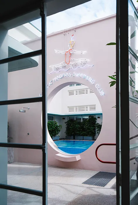 Circular entrance with neon signage for the Madras Swimming Club against a pink wall background.