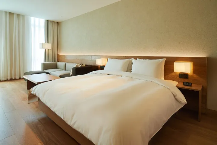 Modern minimalist bedroom featuring a white bed with wood furniture and a wooden floor.