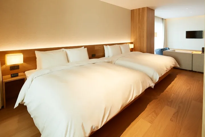 A modern hotel room featuring white beds with wooden headboards and wooden flooring.