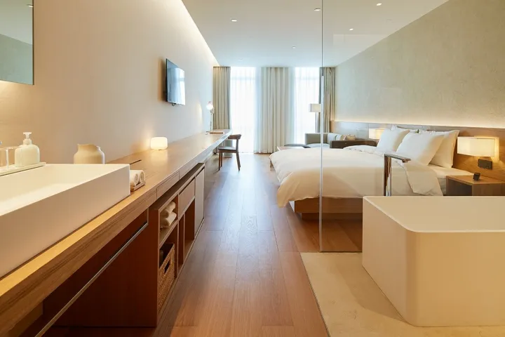 Modern minimalist bedroom with white bed, white walls, and white materials.