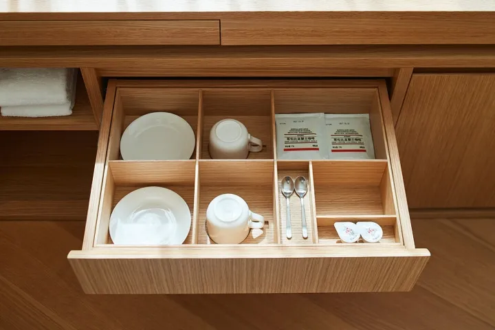 An organized kitchen drawer with compartments containing white ceramics and tea packets.
