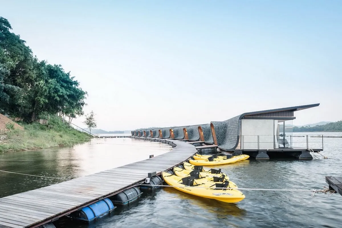 A floating house with a modern design, featuring glass walls and a wooden deck with kayaks.
