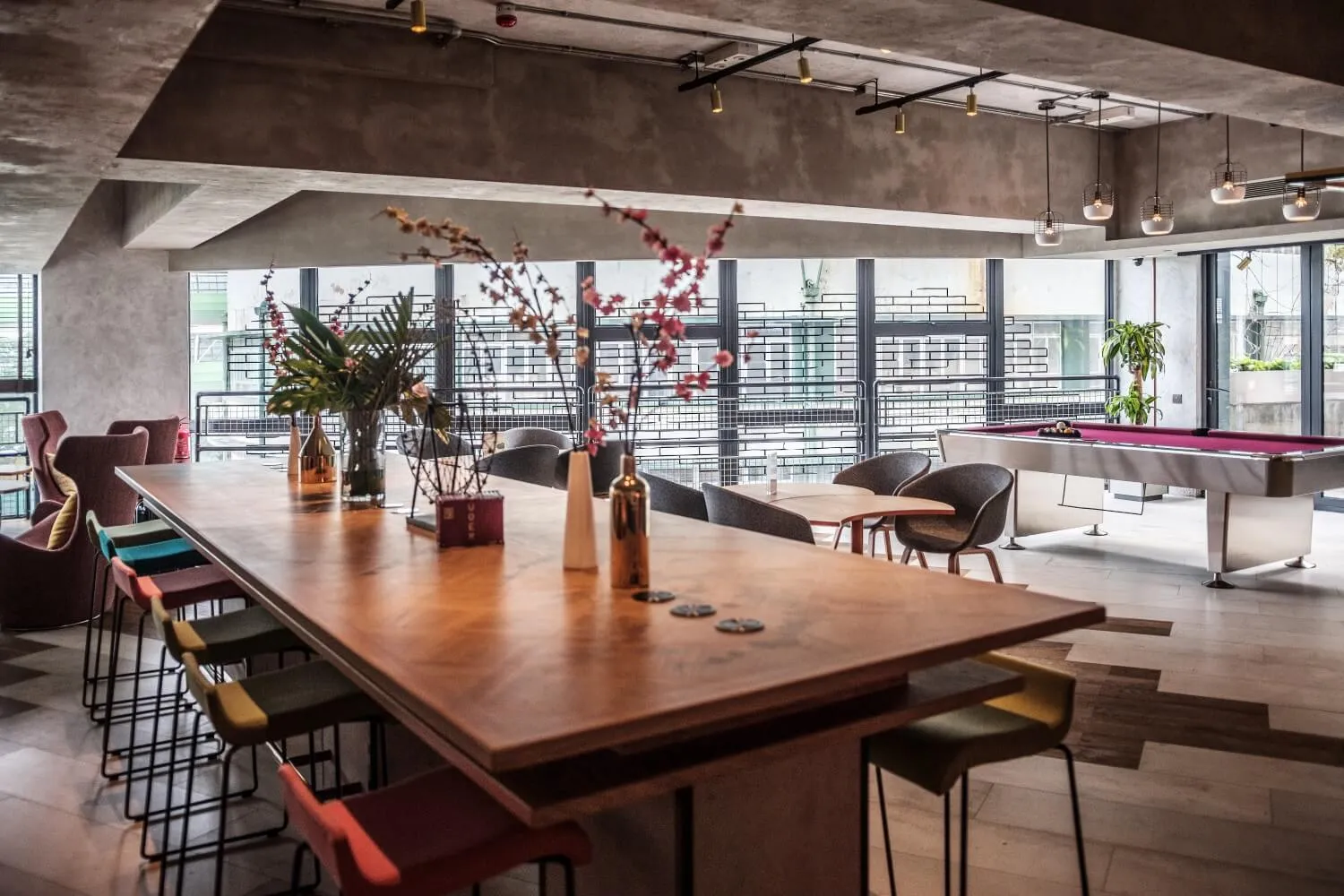 An industrial-style common area with a wooden bar table, concrete ceiling, and bar stools