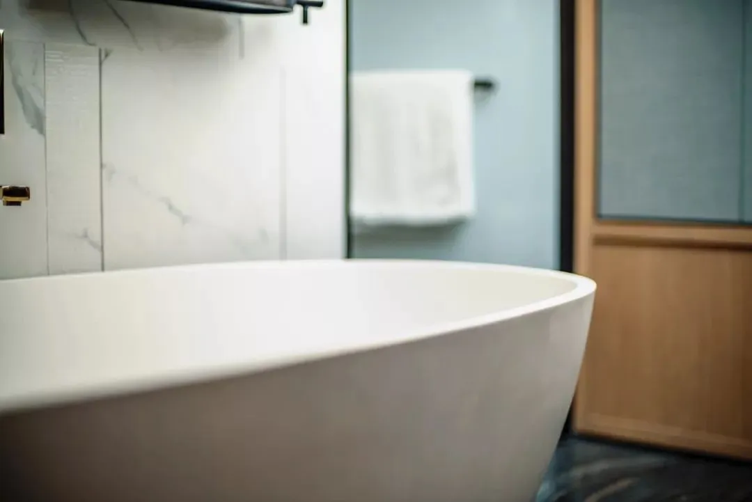 Modern minimalist bathroom with a white ceramic bathtub and marble tiles.