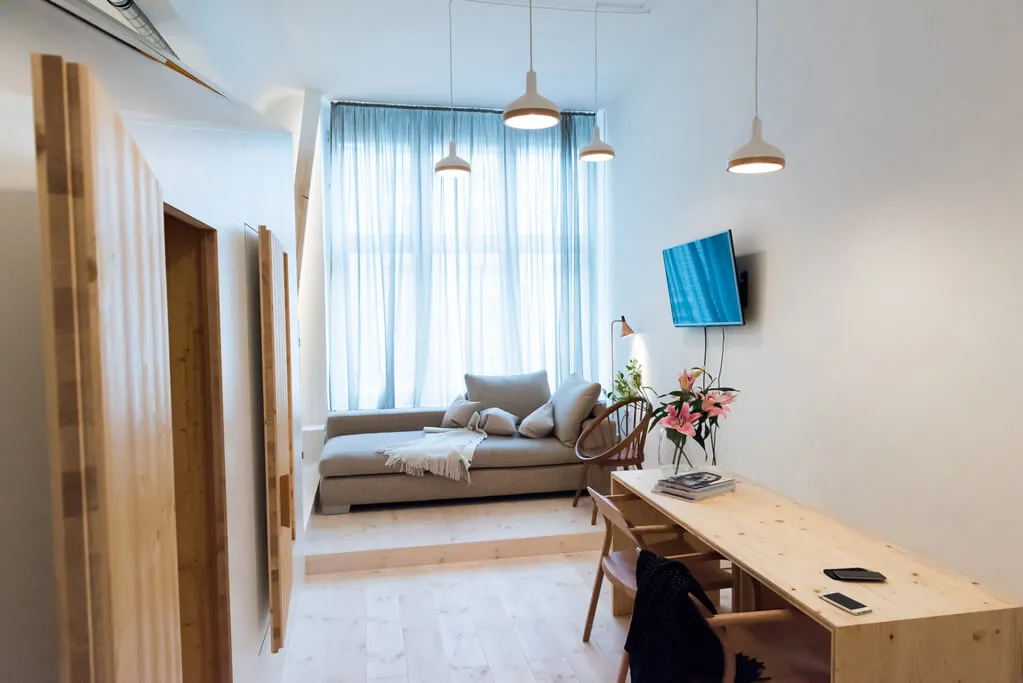 A modern minimalist living room featuring a wooden sofa, glass window, and hanging lamps.
