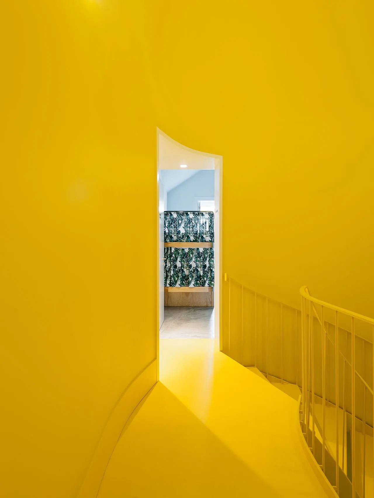 A vibrant yellow stairwell with a curved wall and wooden handrail.