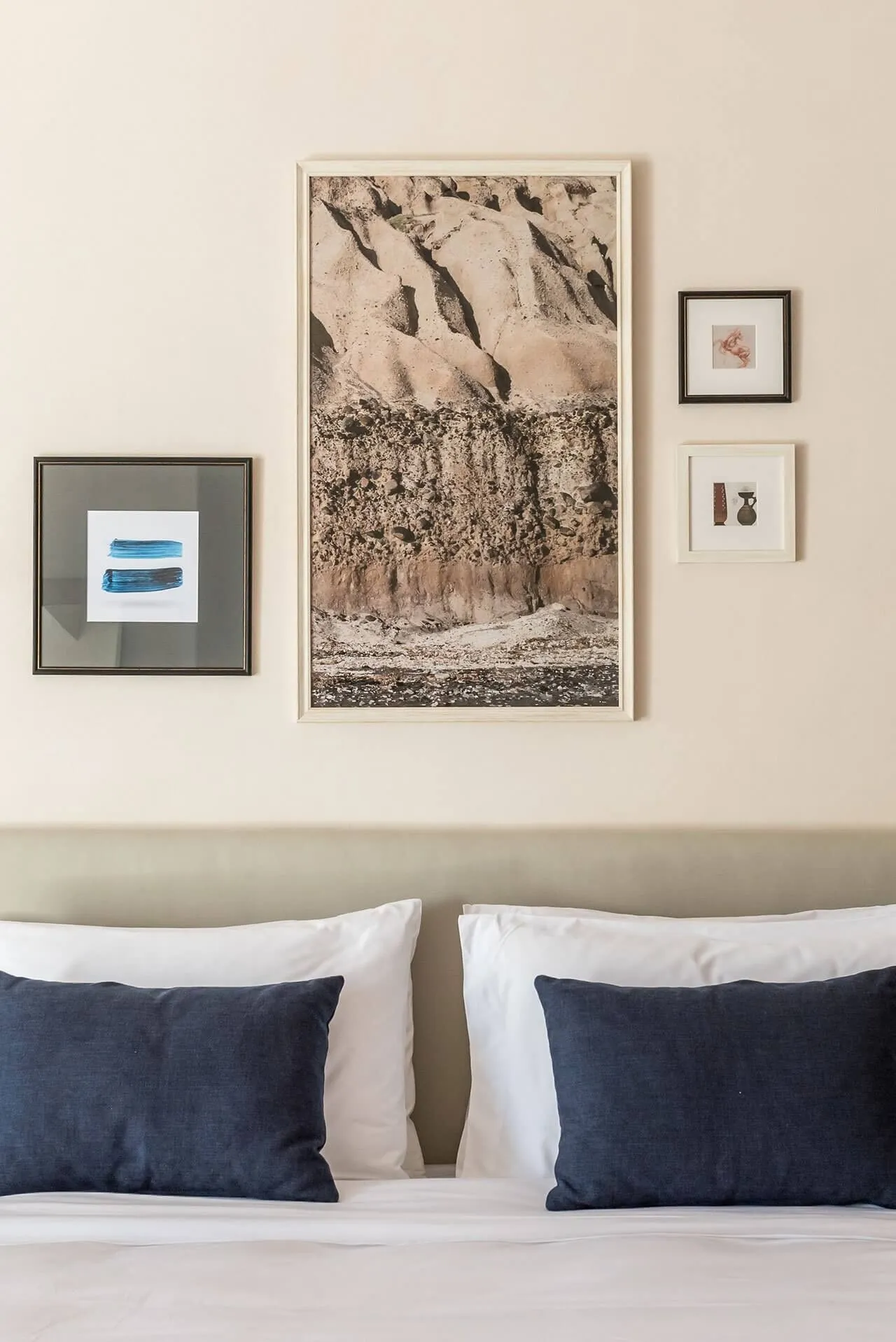 A minimalist bedroom with a framed print of a textured wall on the wall above the bed, complemented by dark blue cushions and