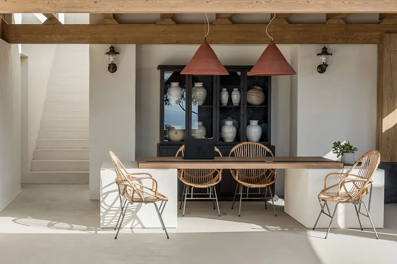 Modern minimalist dining room featuring concrete flooring, rattan chairs, and a wooden dining table.