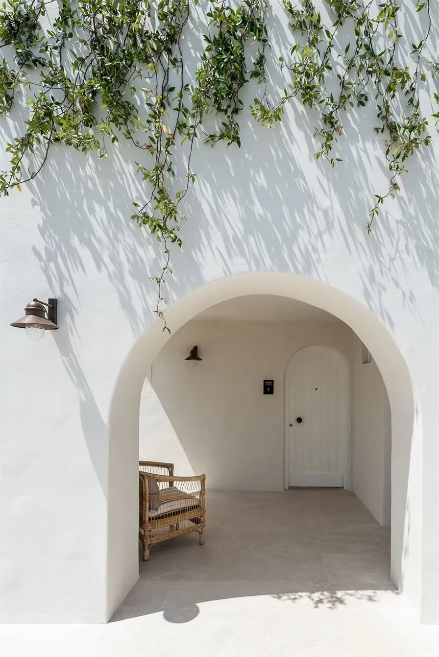 Archway under white wall with vines hanging down and a rattan chair.