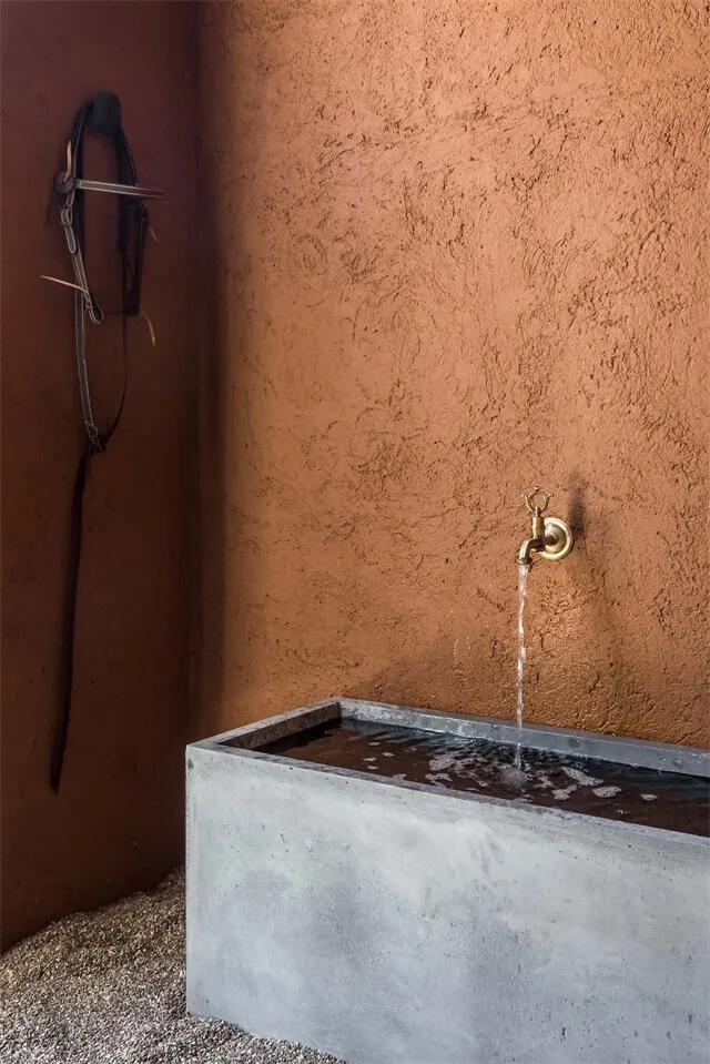 Concrete water feature with a brass faucet pouring water into a pool against a textured wall, minimalist design