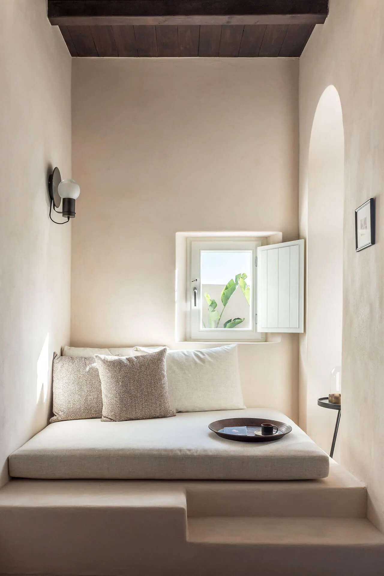 A minimalist living space with light-colored concrete and covered seating area with cushions and pillows.