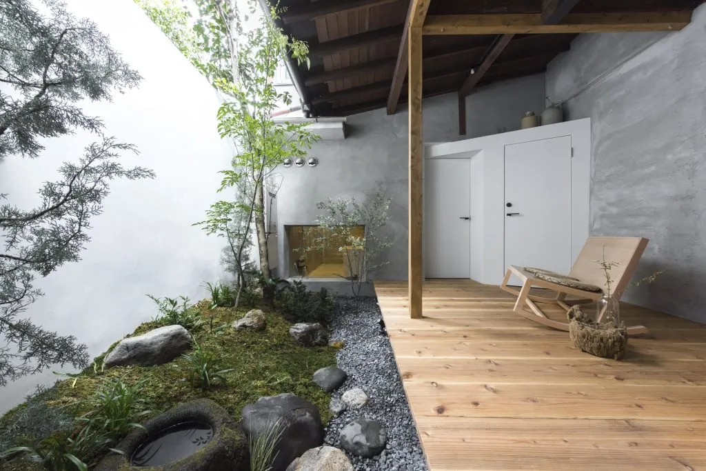 A minimalist verandah interior with wooden flooring, concrete walls, and plants.