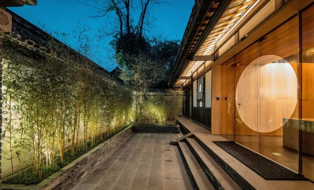 Modern residential entryway with wood flooring, lighting, and a circular glass door.