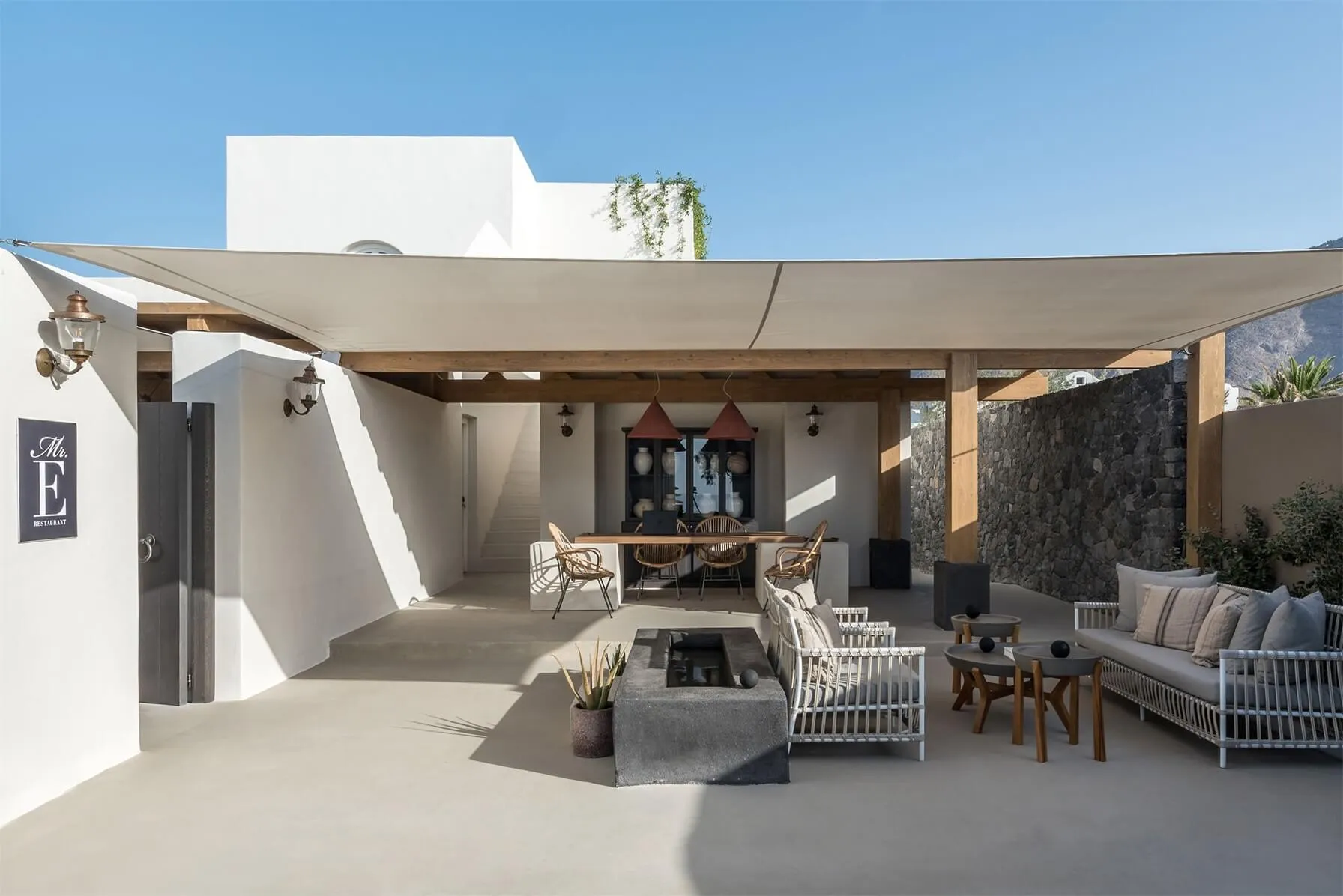 A modern, minimalist patio featuring concrete flooring, a fire pit, and outdoor seating.