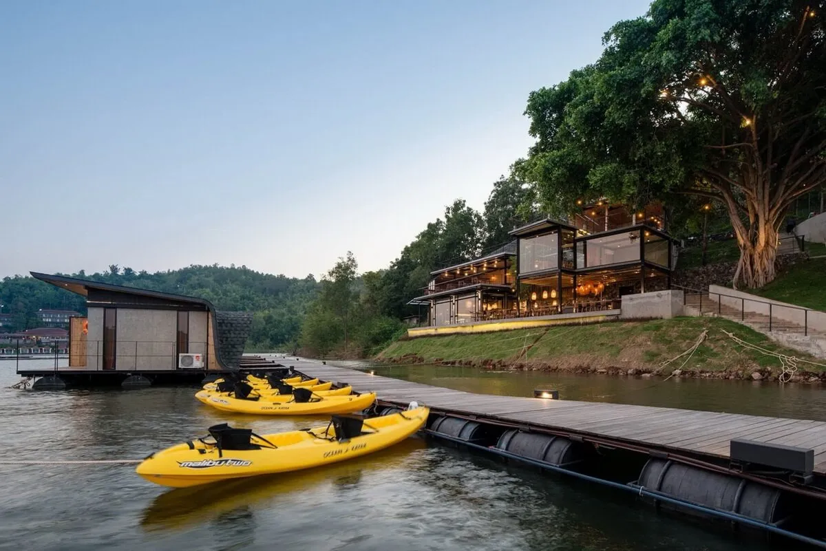 Modern resort lodge with concrete and glass exterior, featuring wooden dock and kayaks.